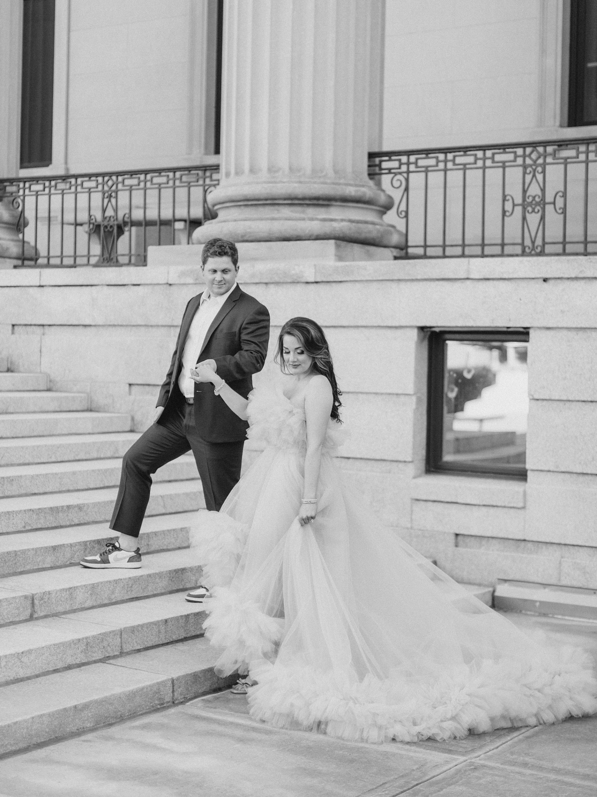 groom leads bride up steps of Charlotte courthouse during glam Charlotte engagement session