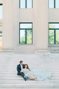 bride in glamorous blue dress leans into groom sitting on steps during glam Charlotte engagement session