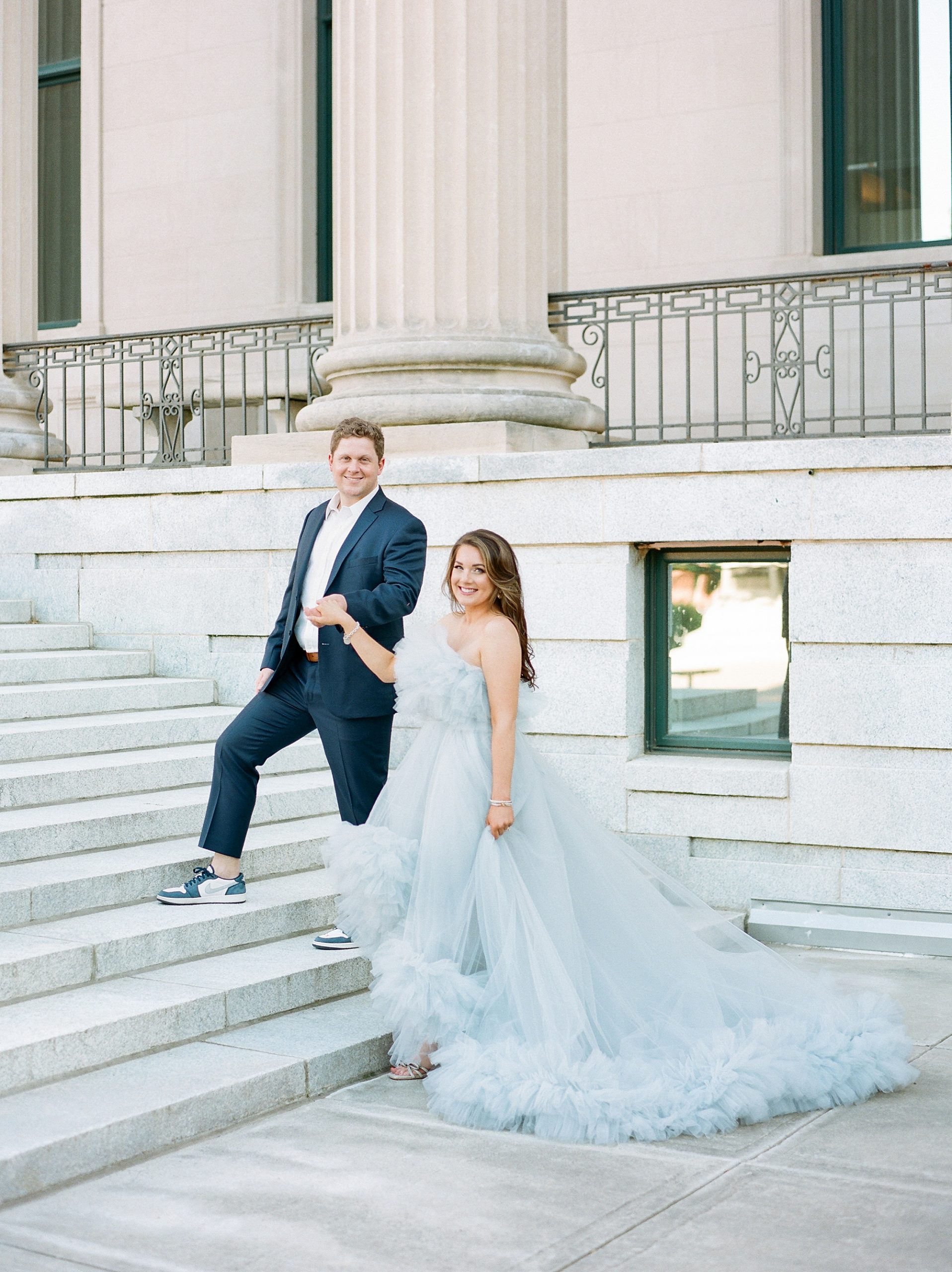 man leads woman in light blue gown up steps during glam Charlotte engagement session