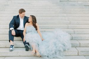 engaged couple sits on steps of Charlotte courthouse with bride's dress around her