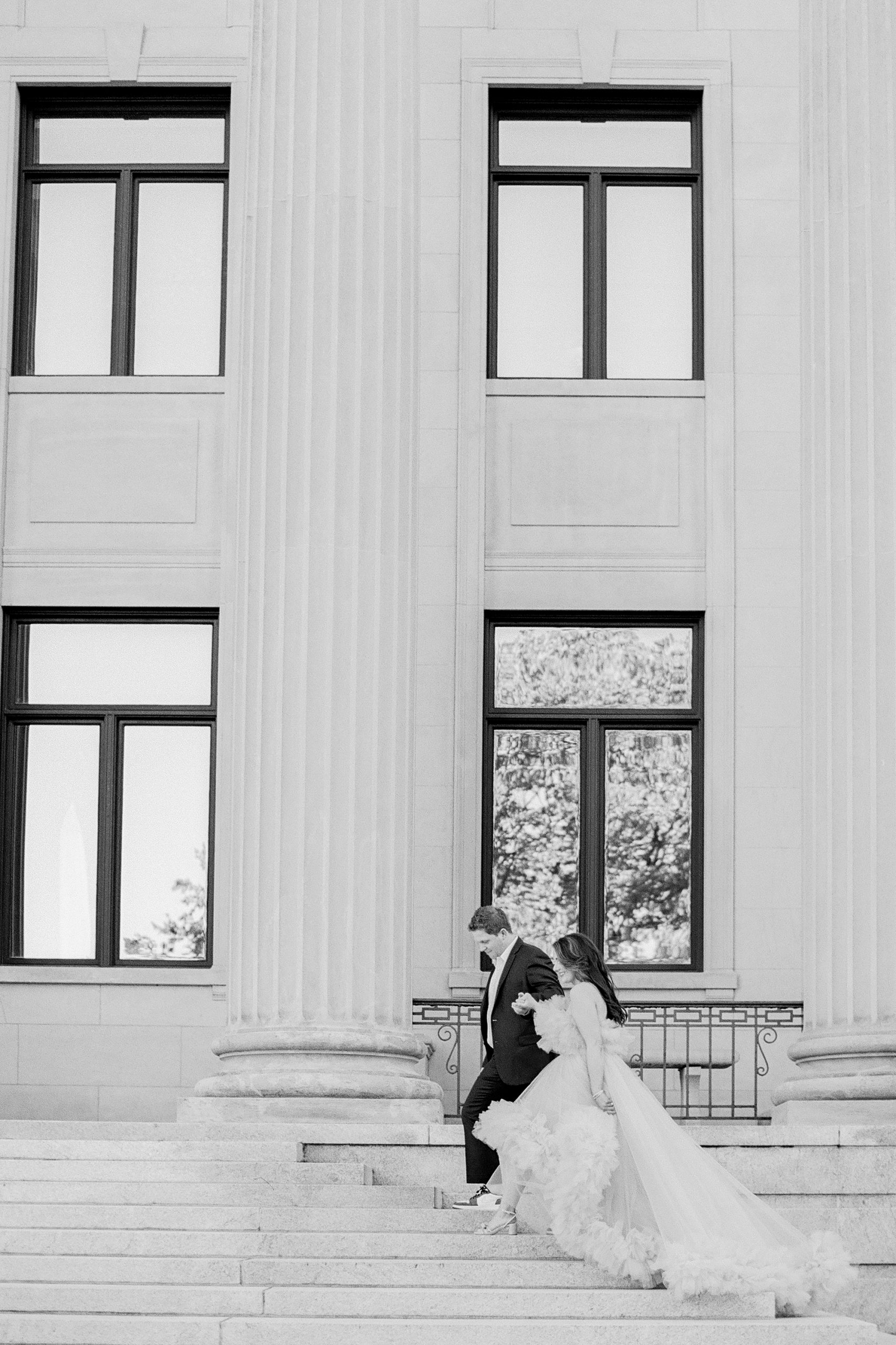 engaged couple walk up steps of courthouse with bride in glamorous gown