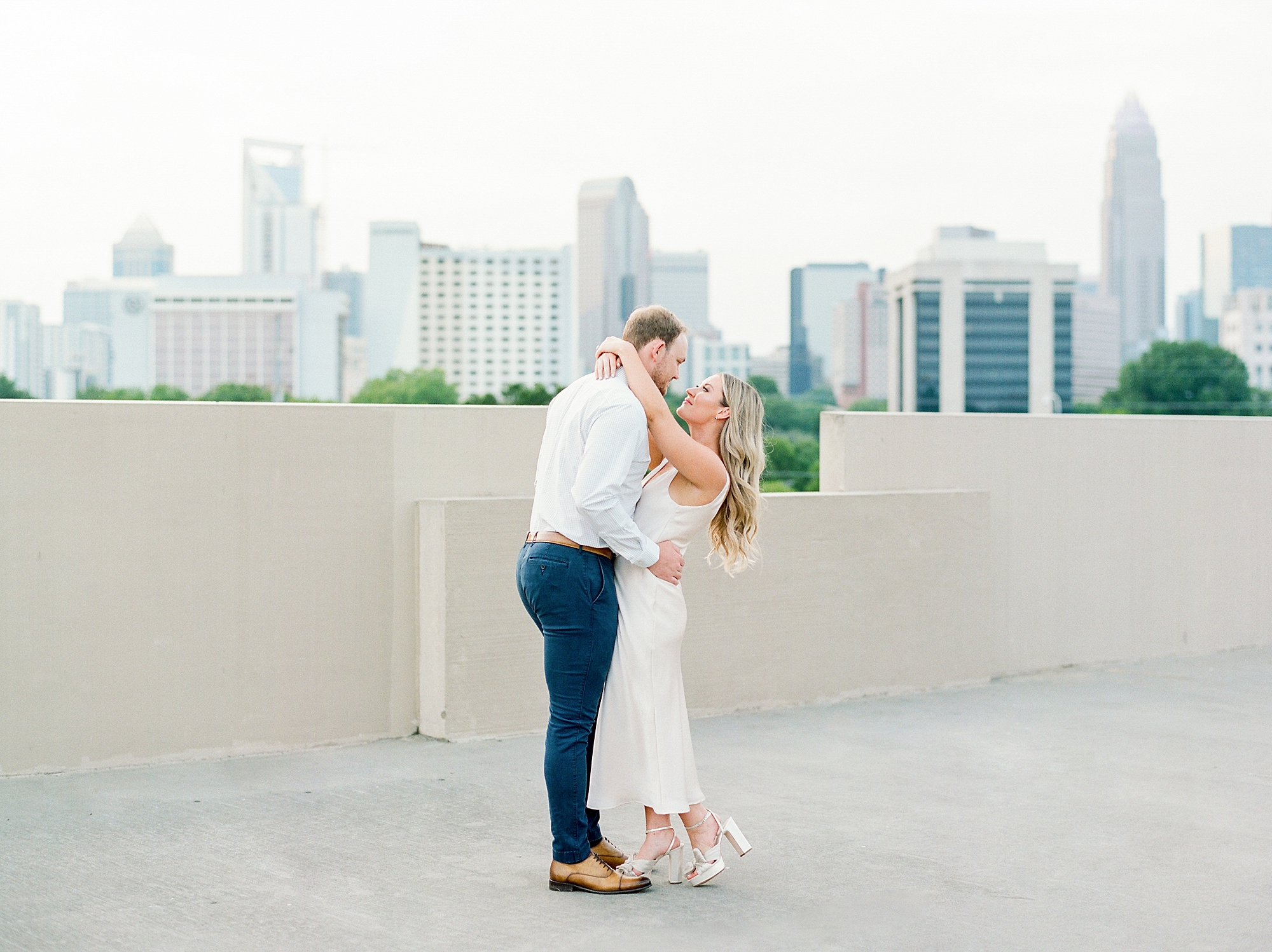 couple hugs on rooftop with Charlotte skyline behind them