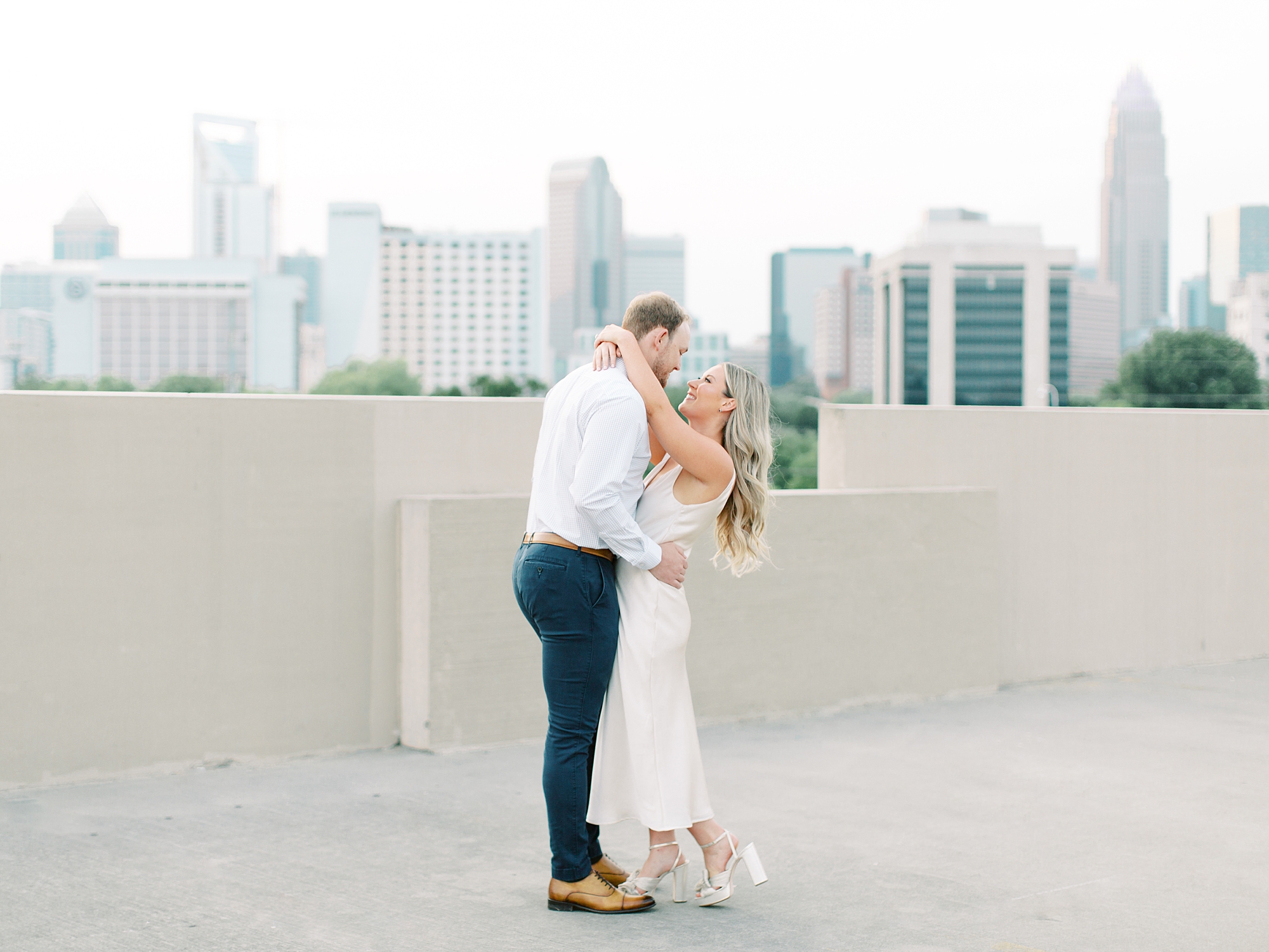 engaged couple hugs on rooftop during Uptown Charlotte engagement session