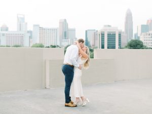 engaged couple stands on rooftop kissing
