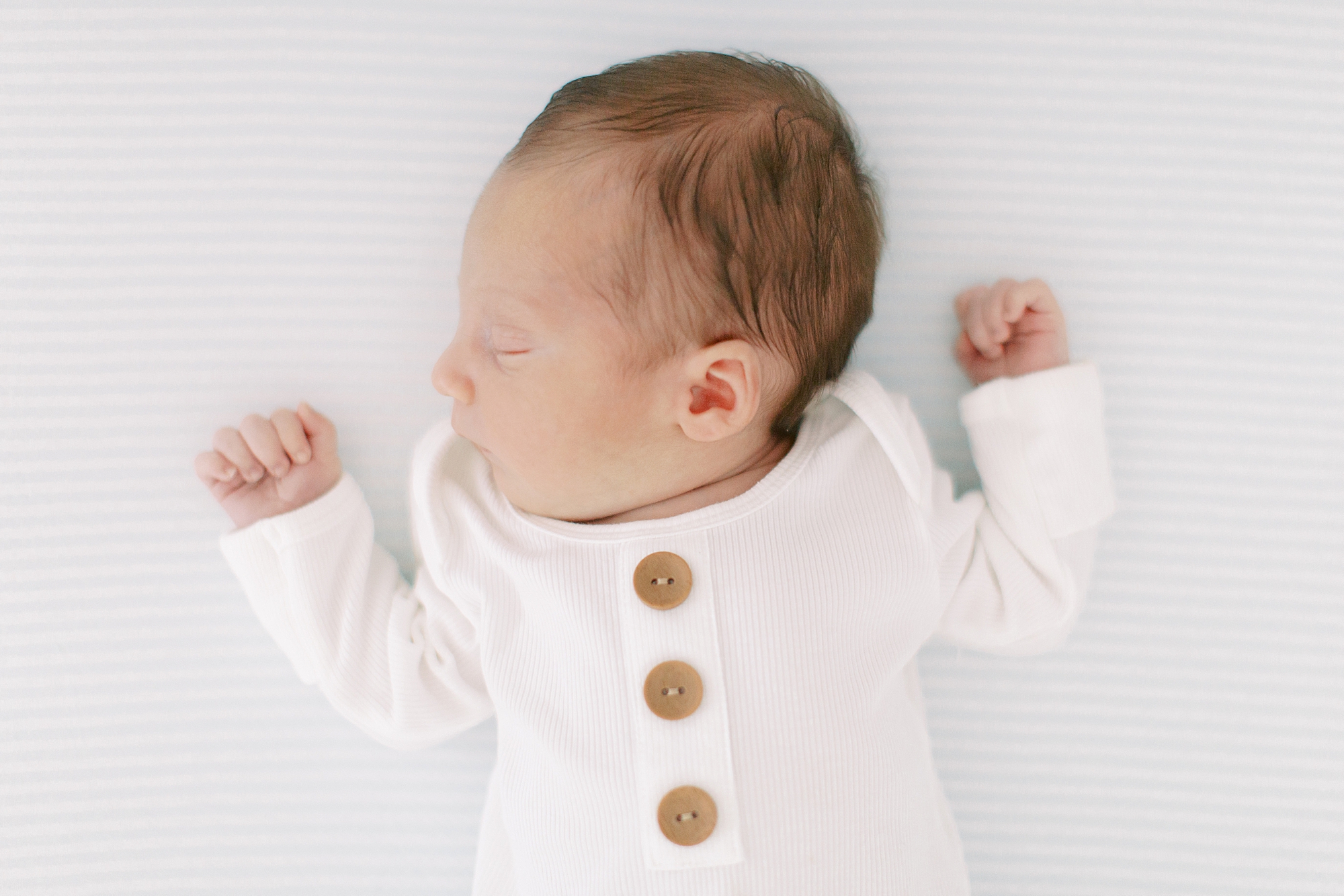 baby boy sleeps in white onesie with brown buttons