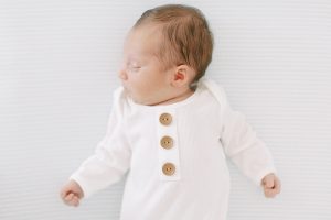 baby boy sleeps in white onesie with wooden buttons