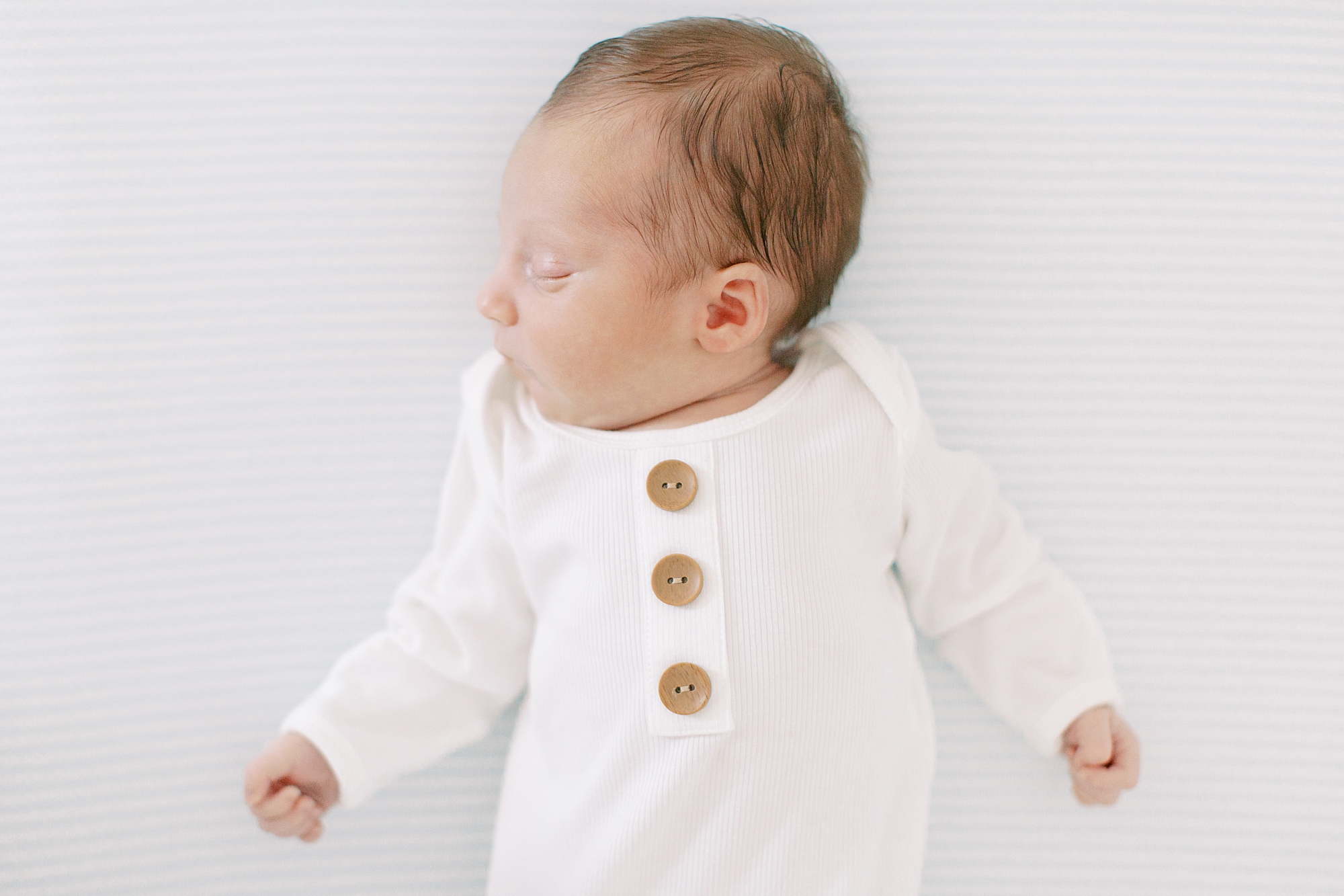baby boy sleeps in white onesie with wooden buttons
