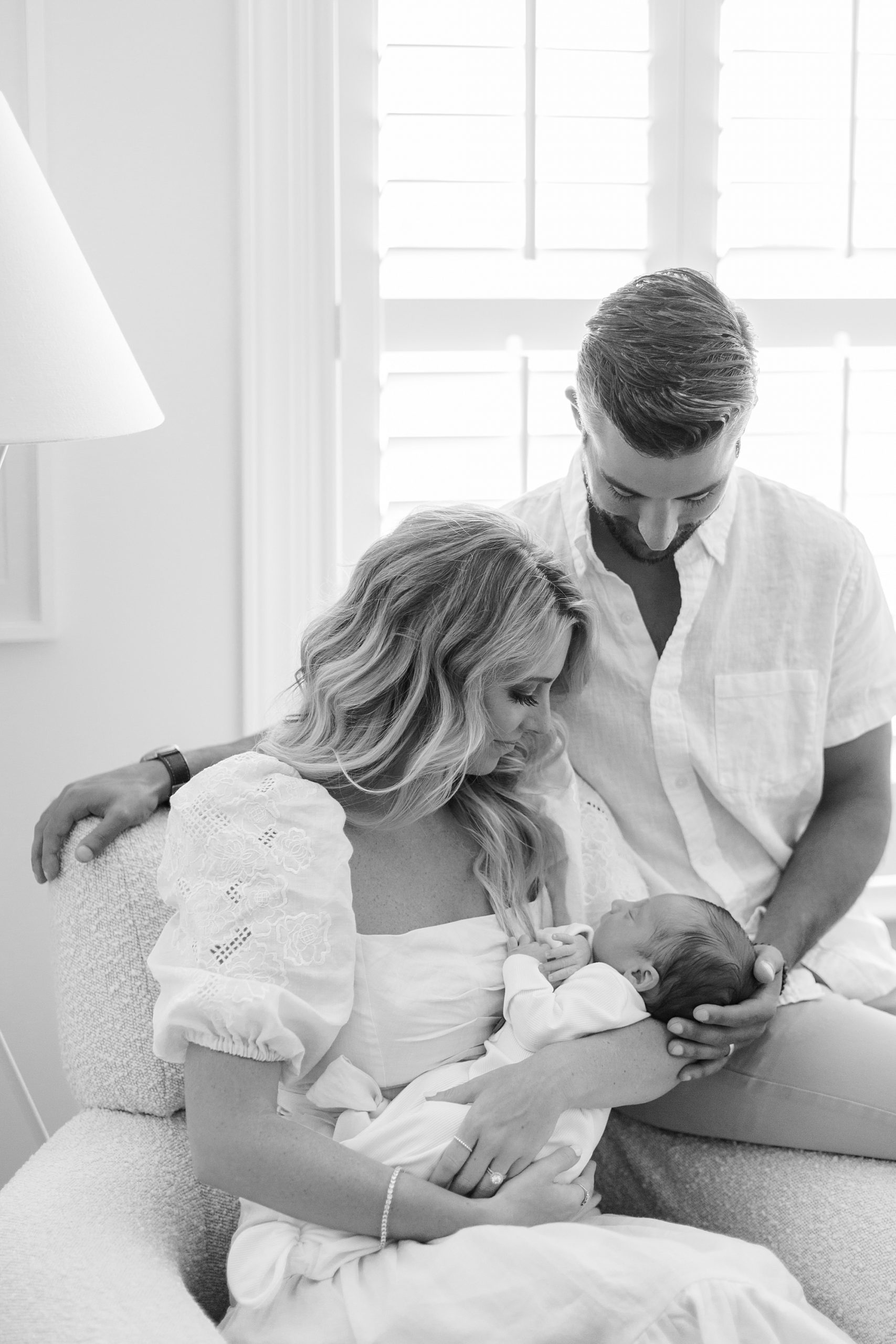 mom and dad look down at baby boy during newborn photos in nursery