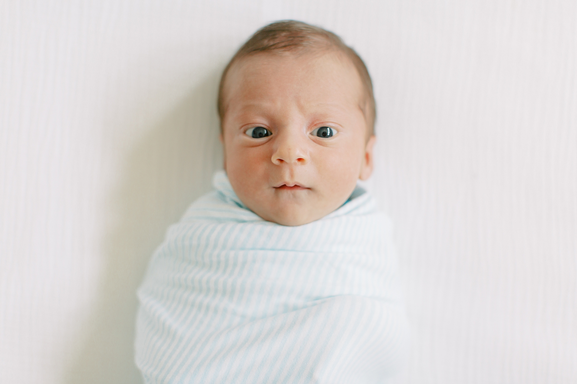 baby lays in blue swaddle with eyes open