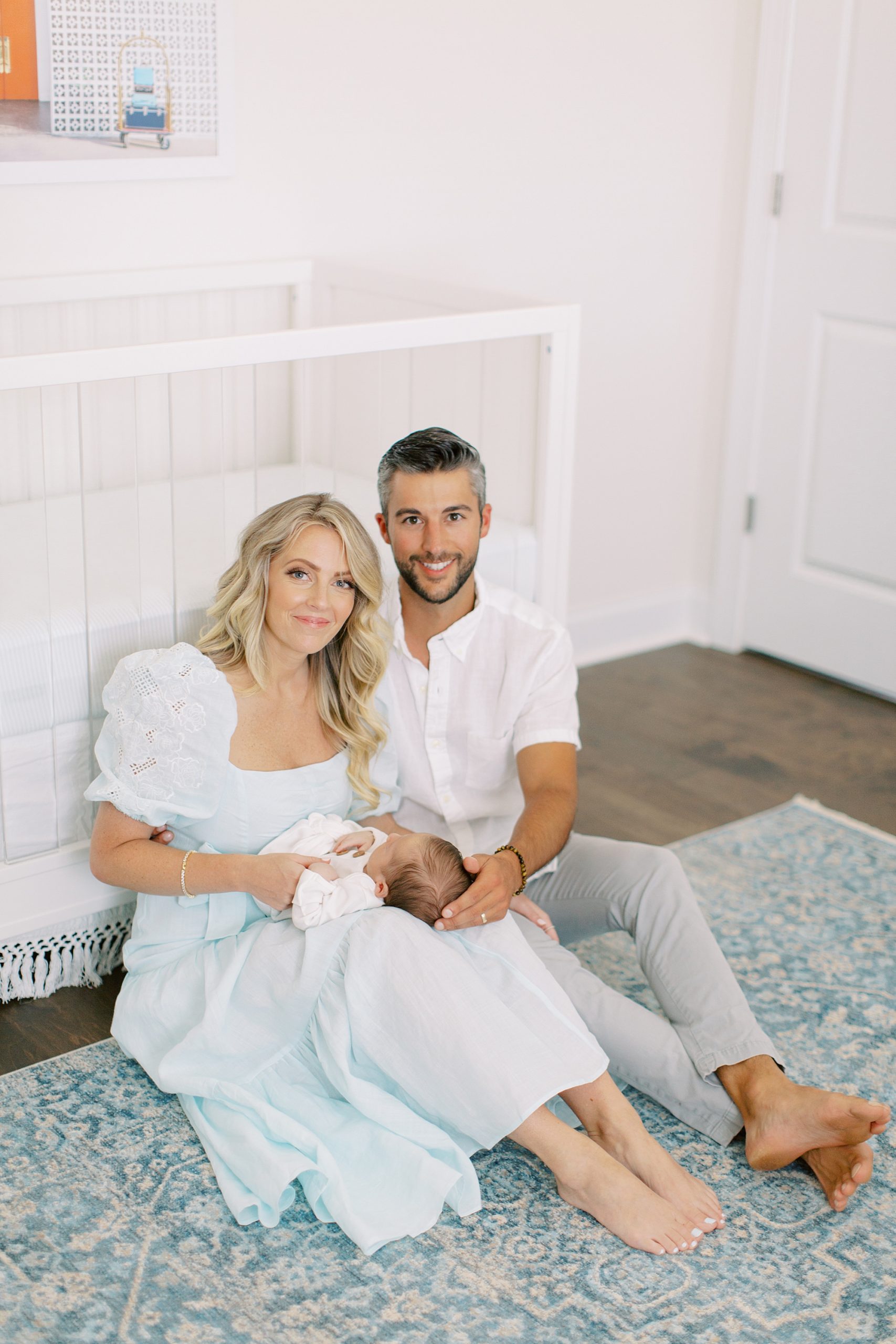 parents sit against crib holding new baby boy during lifestyle photos