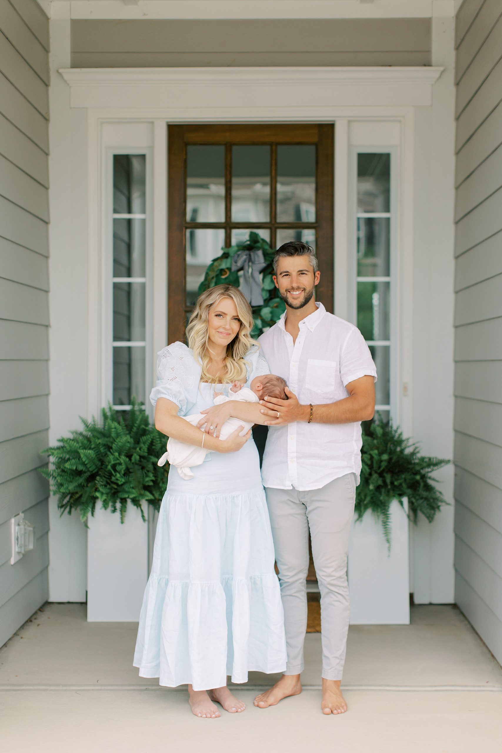 parents stand on front porch with son during Charlotte lifestyle newborn session