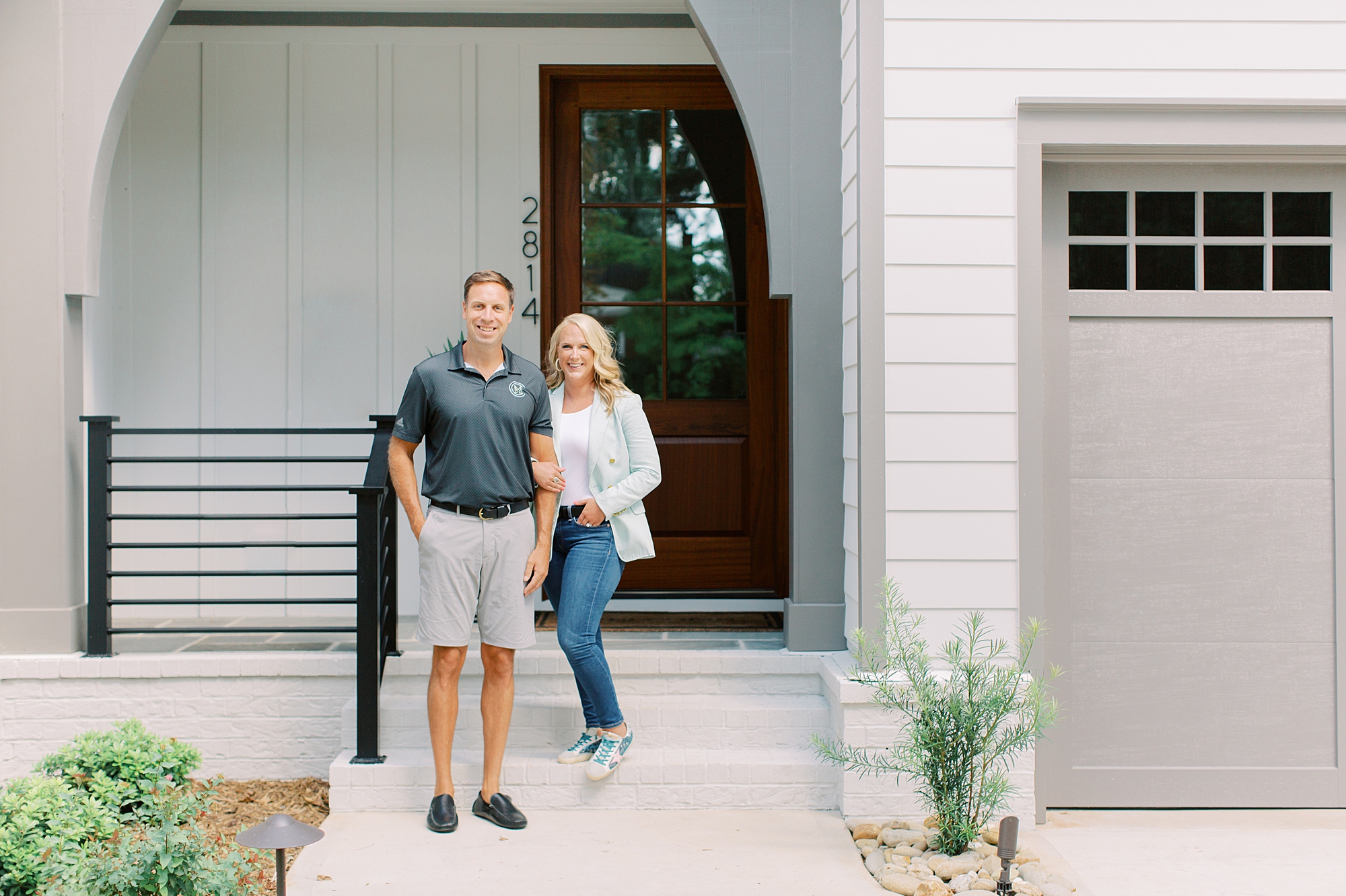 husband and wife team stand on front porch during Charlotte branding portraits for construction company