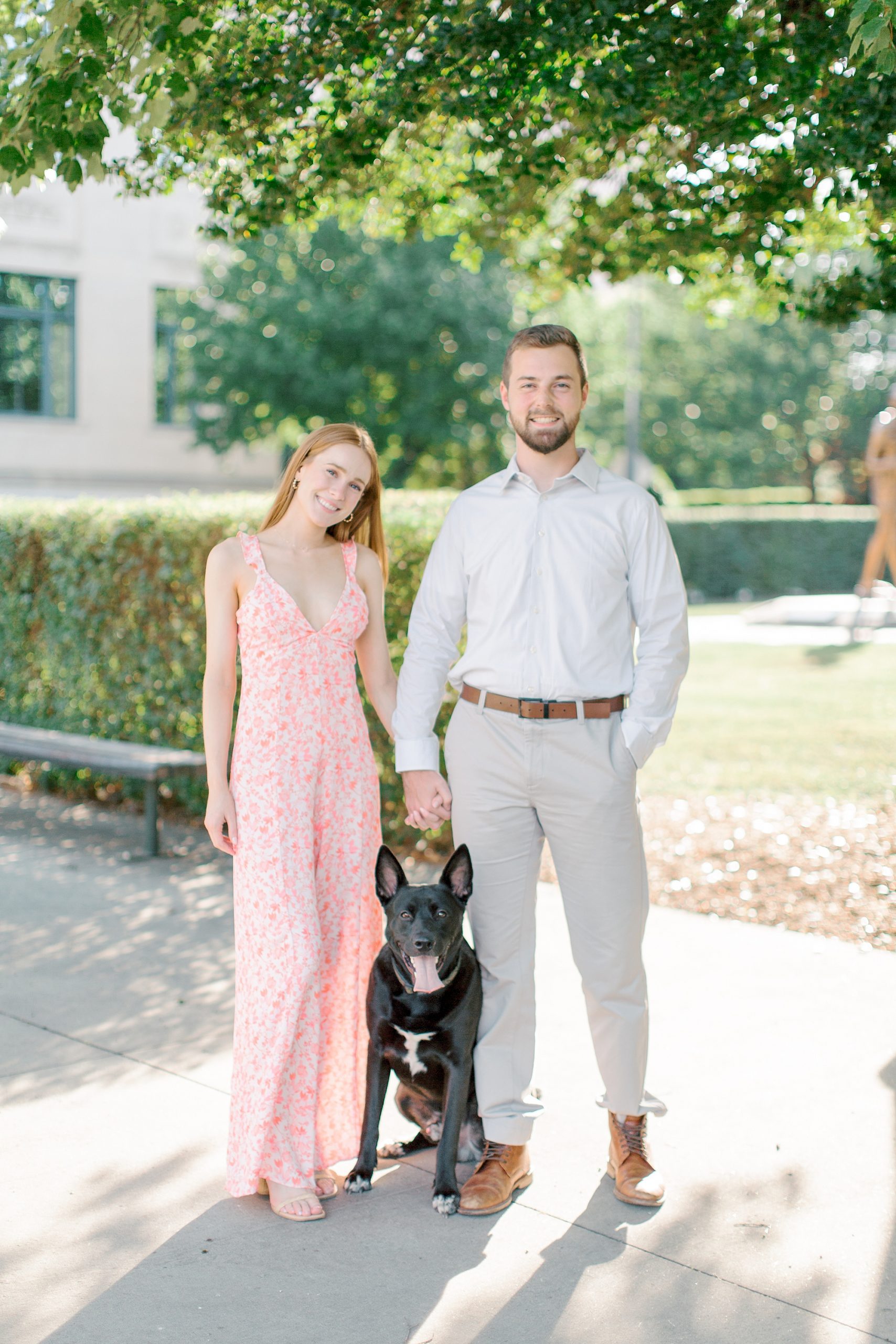 engaged couple stands with dog during Uptown Charlotte engagement session