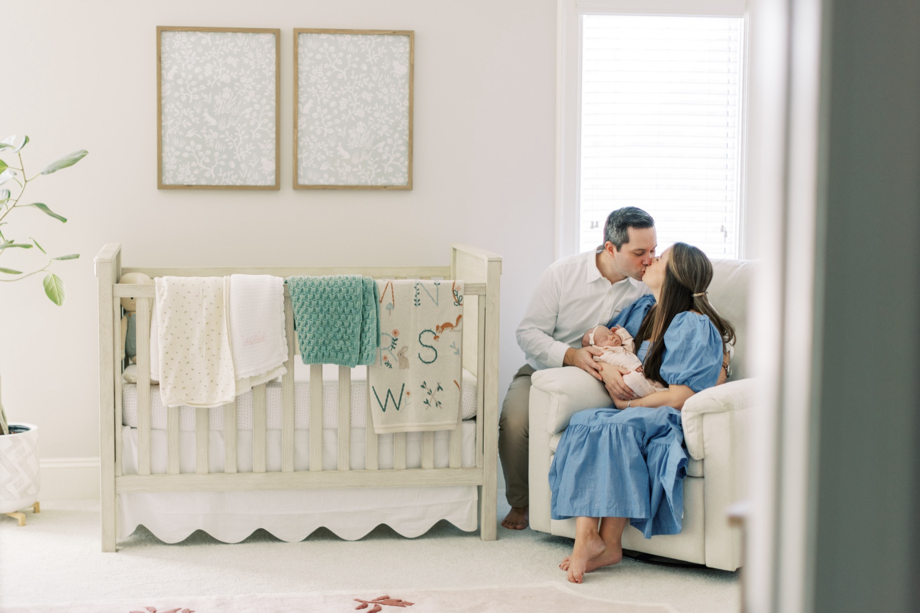 parents kiss holding newborn between them in rocker during newborn session In Charlotte home nursery