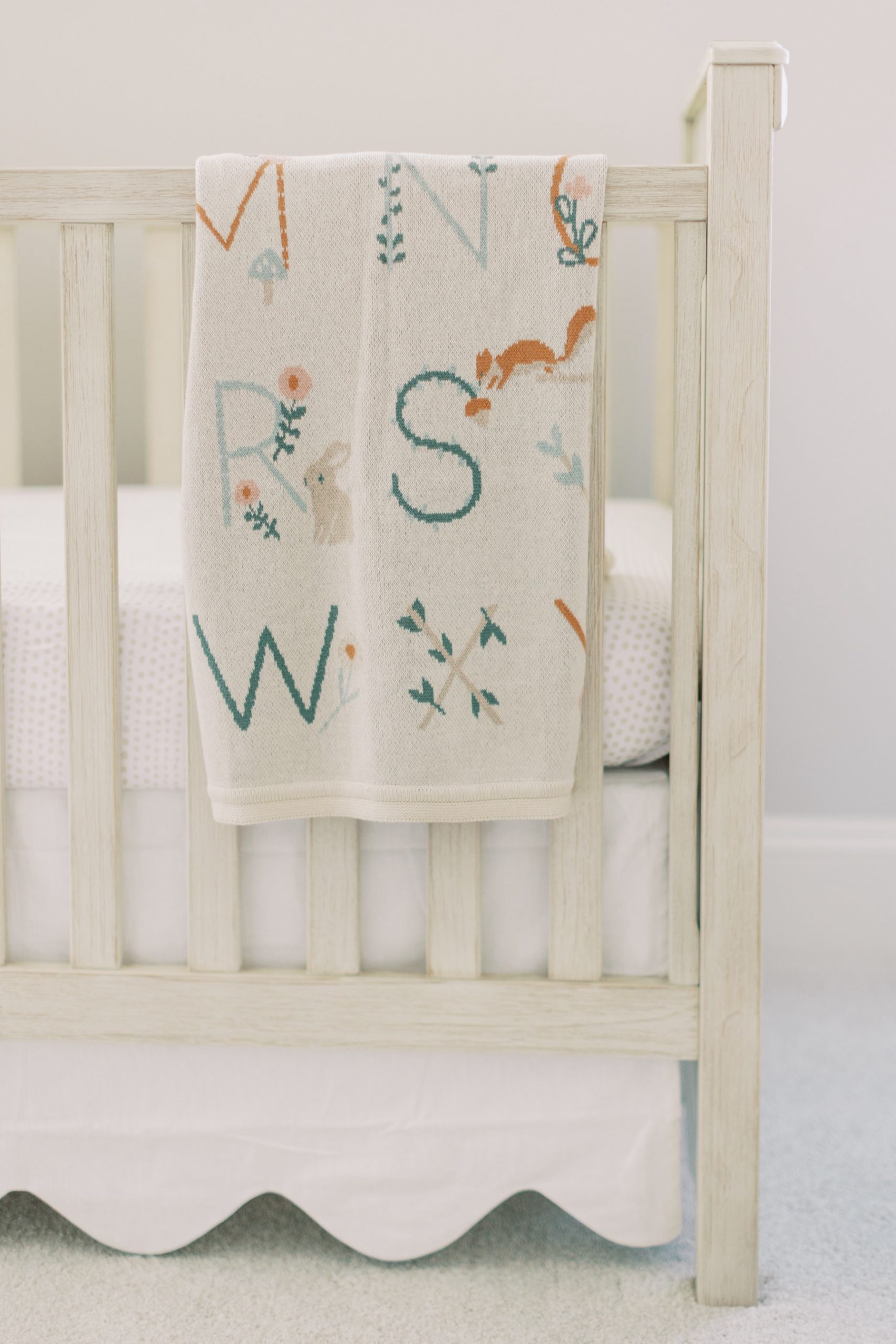 neutral hand sewn alphabet blanket hangs on ivory crib in Charlotte nursery