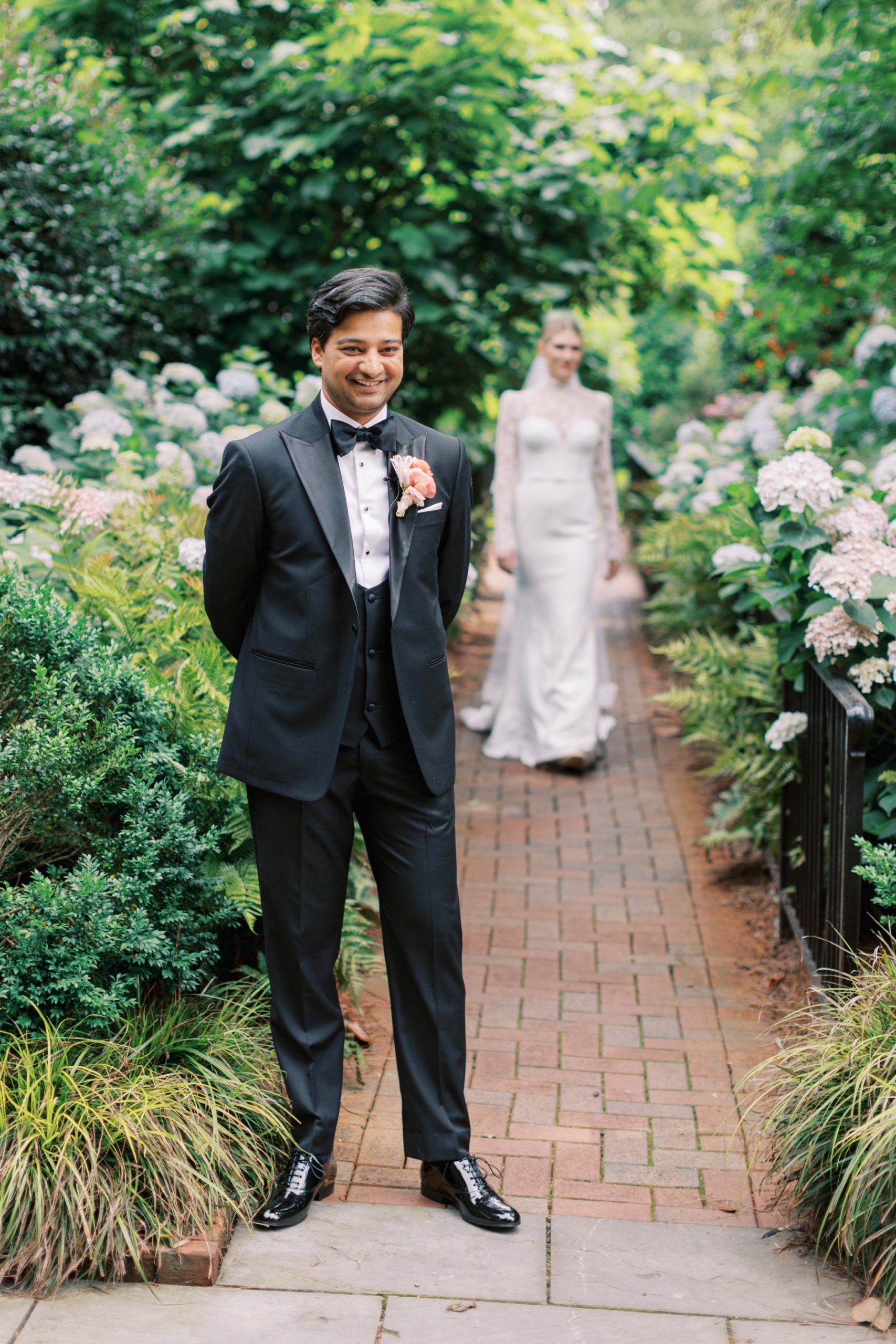 groom grins waiting for bride for first look in gardens of Duke Mansion