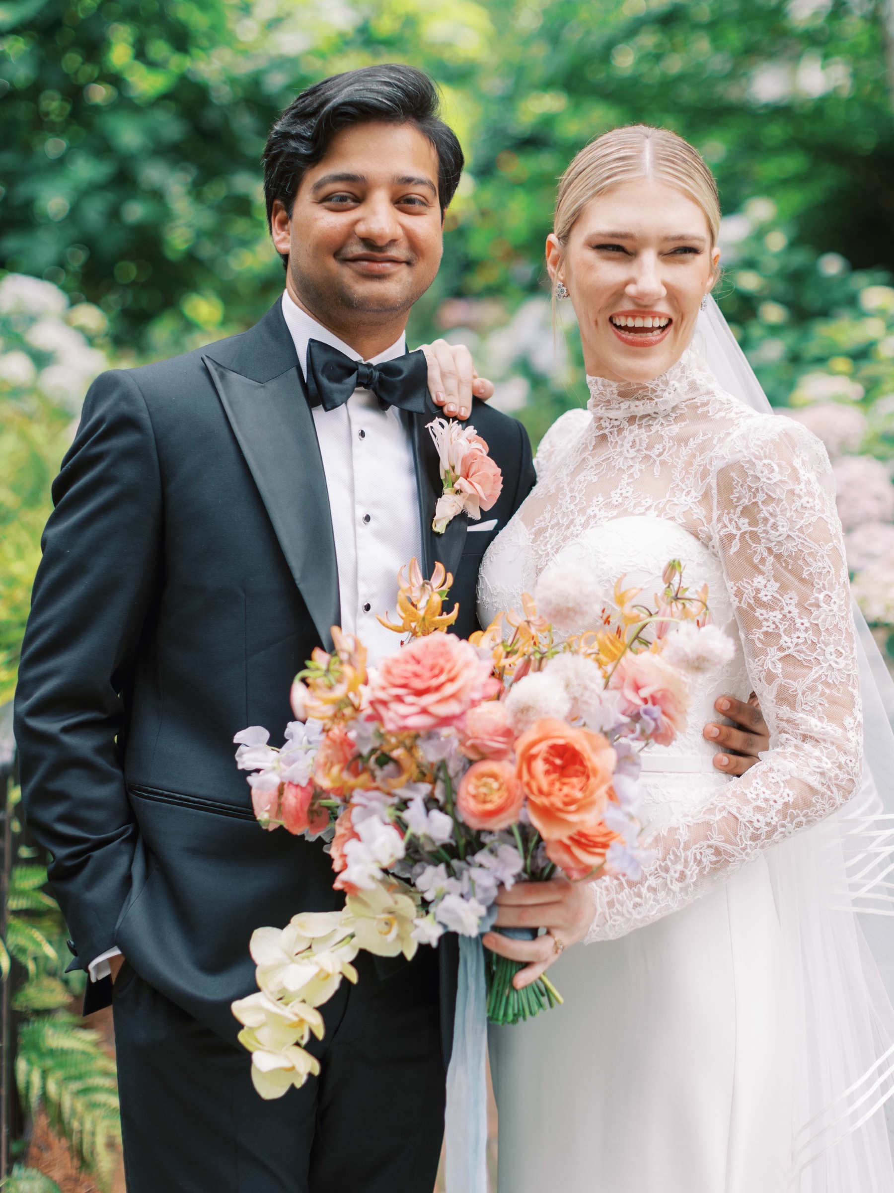 bride laughs holding groom's shoulder while posing with colorful bouquet 