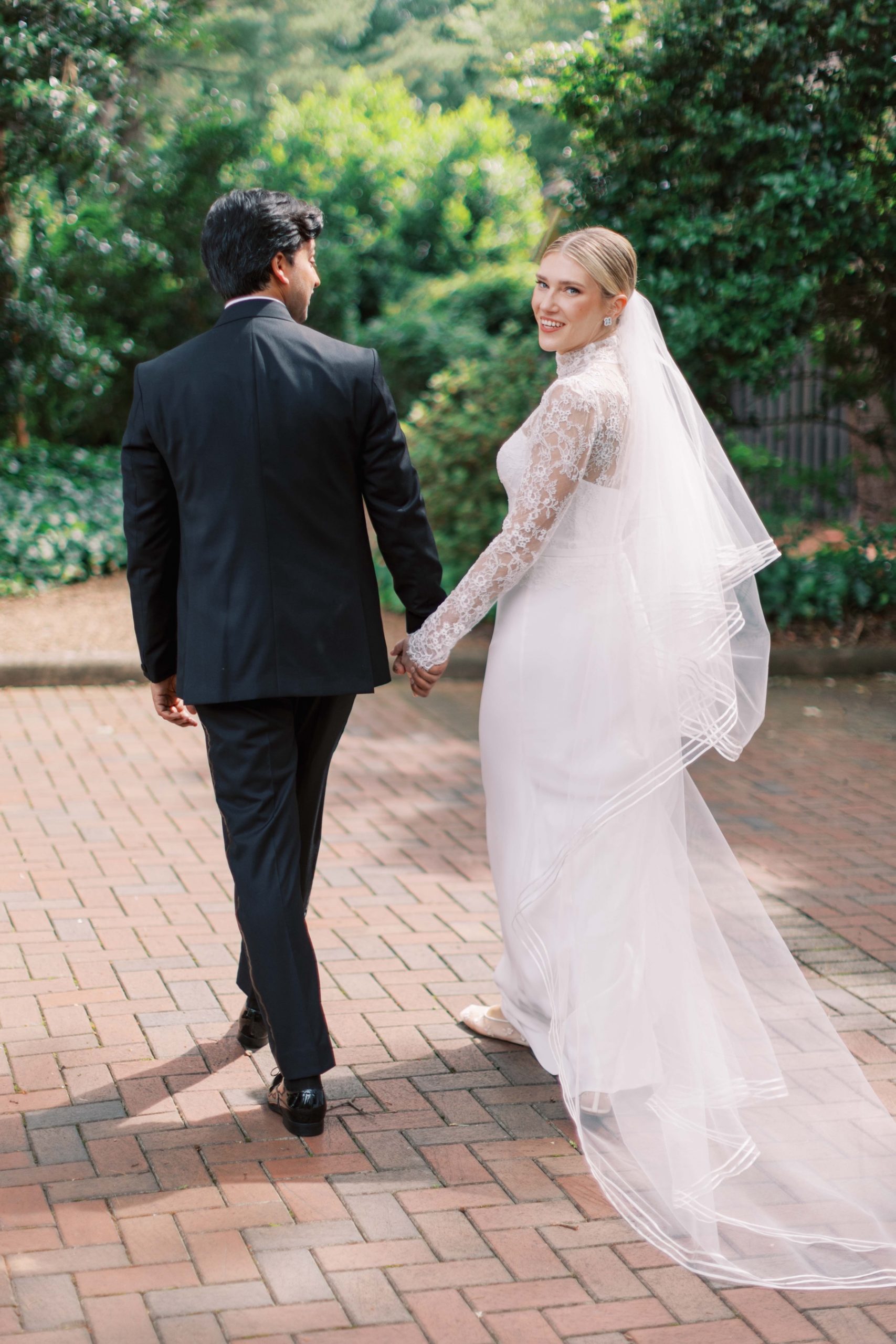 bride and groom hold hands walking through gardens of Duke Mansion