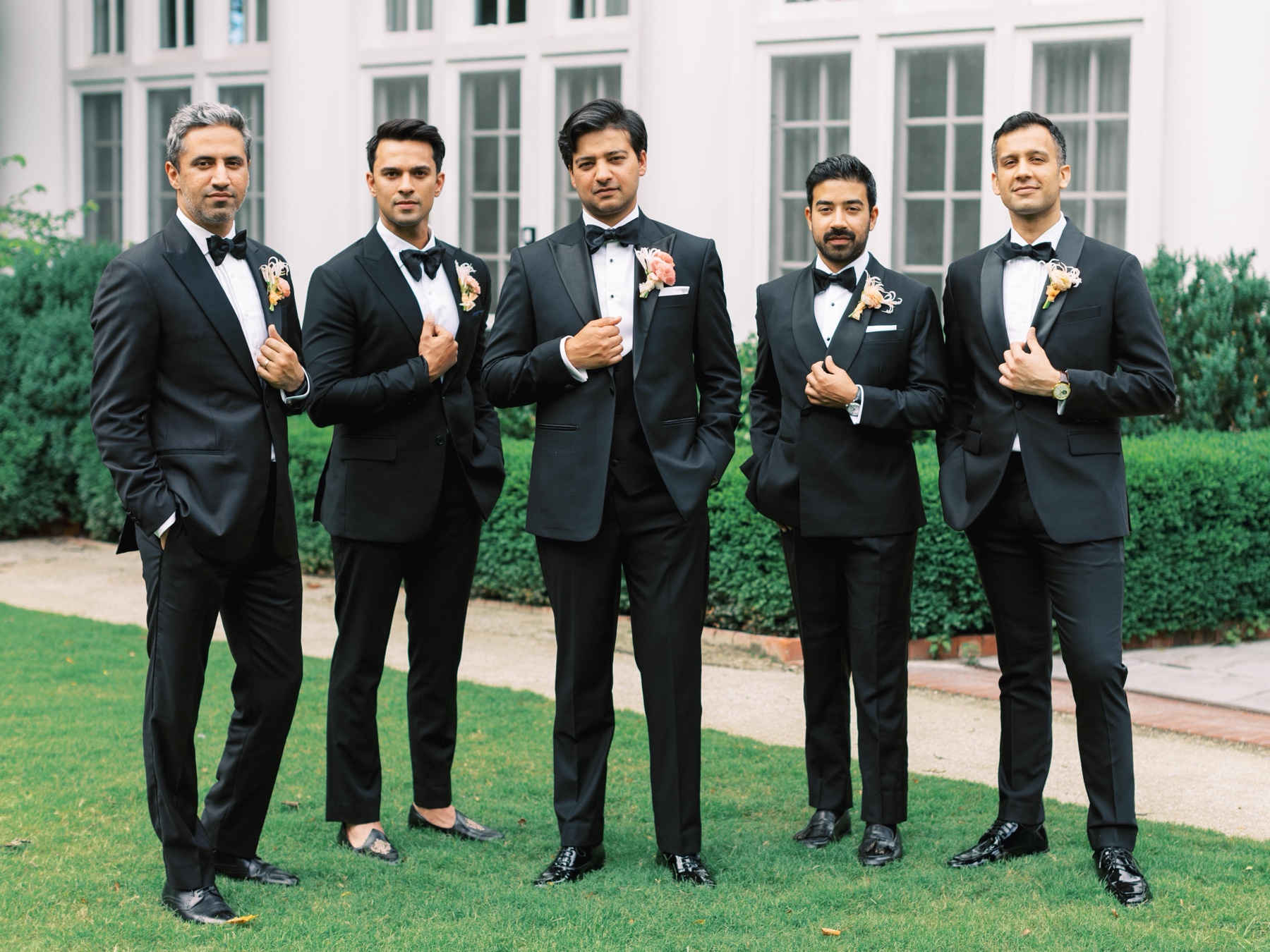groom and groomsmen stand holding lapel of suit jacket standing on the lawn outside Duke Mansion 