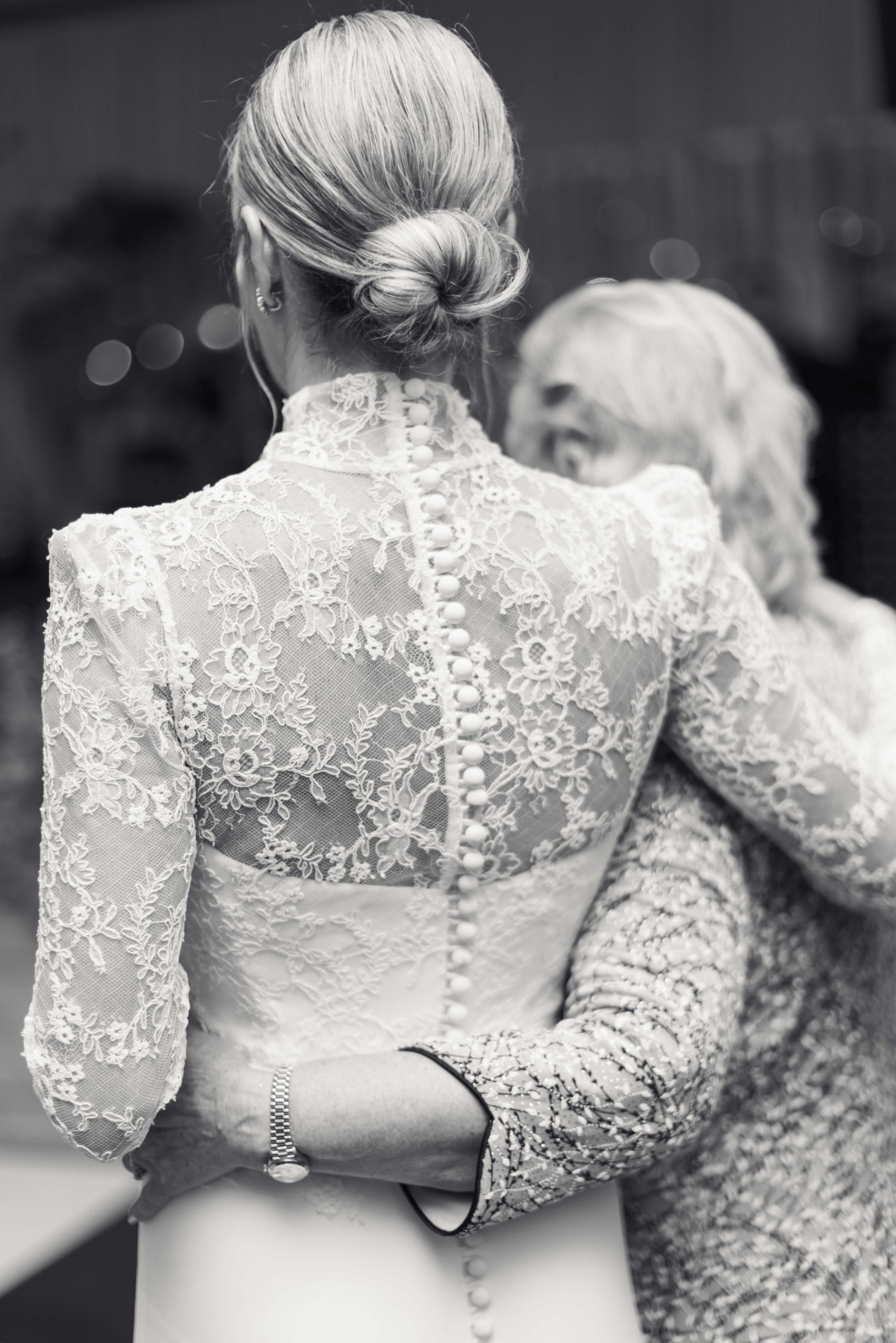 black and white photo bride hugging mother showing off pearl buttons on dress