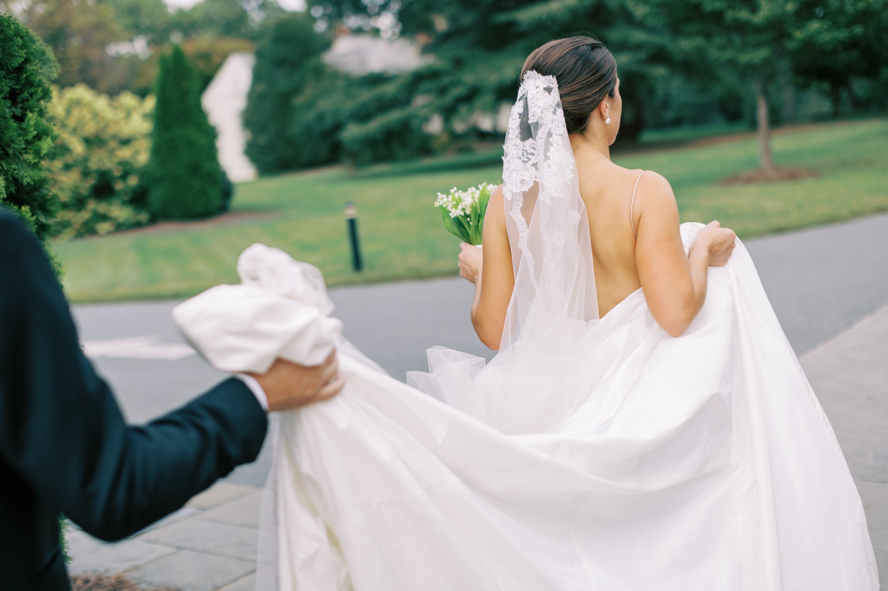 bride walking as groom holds up the back of dress