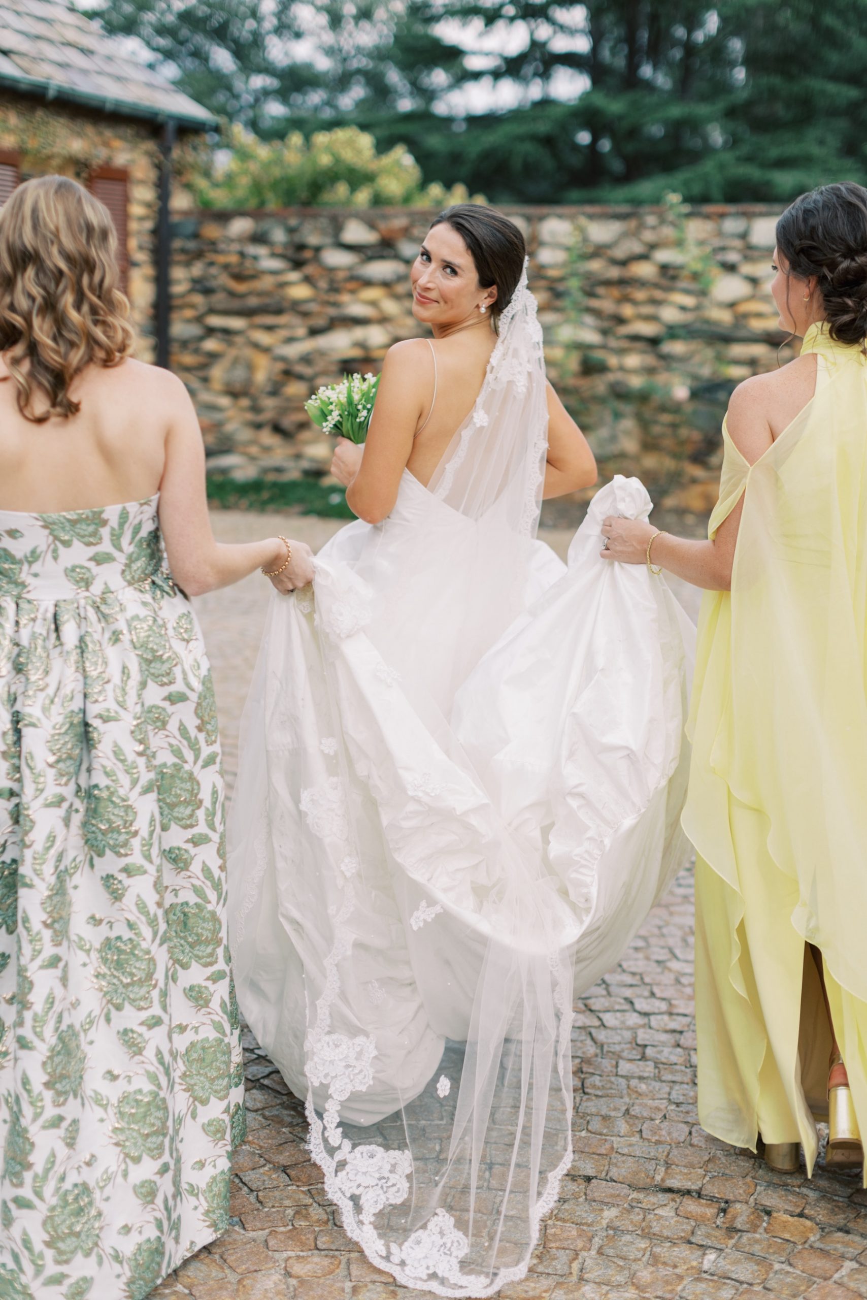 bridesmaids walk next to bride and hold up the back of her dress